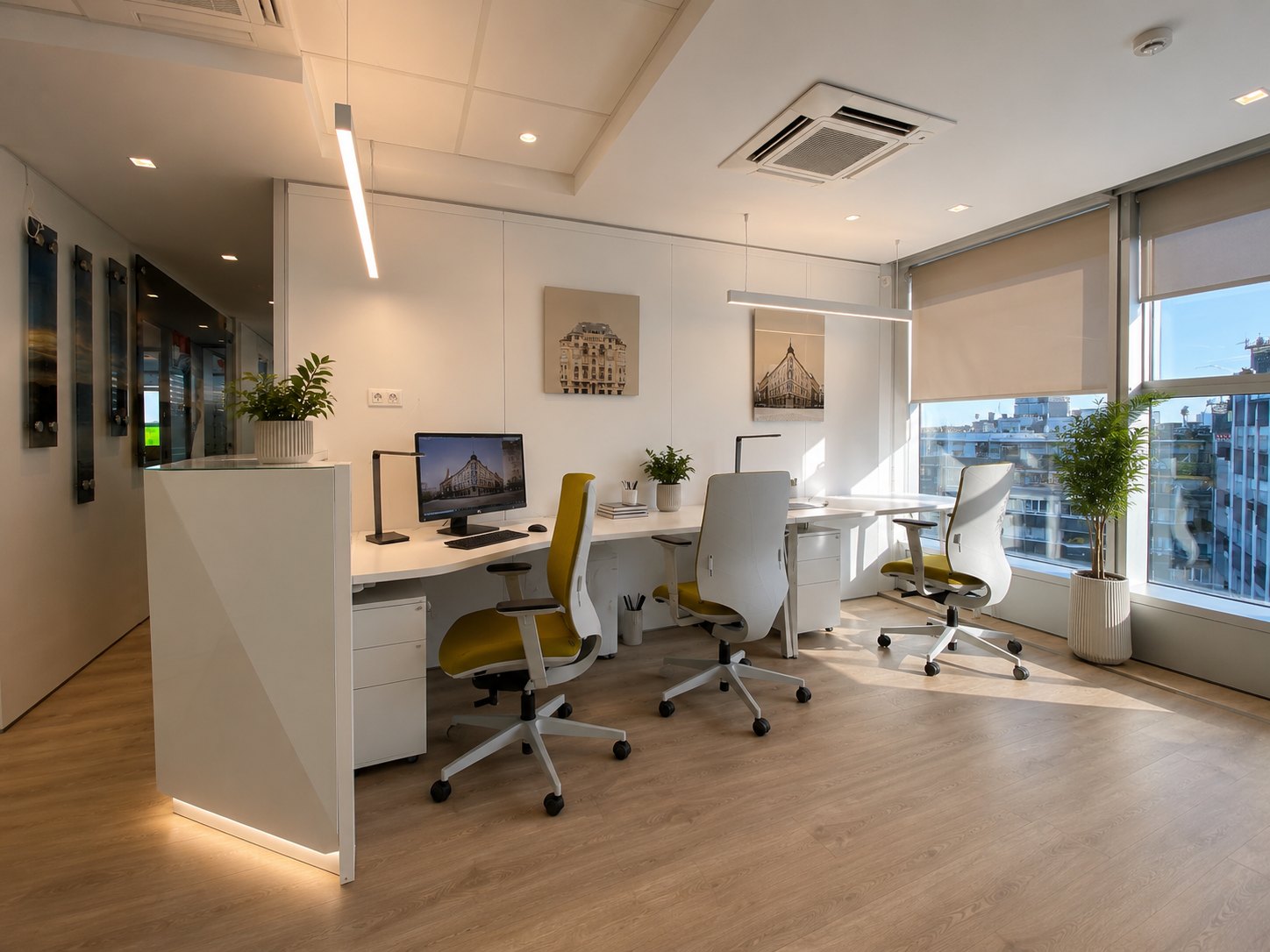 Three workstations with white desks and yellow-green chairs, building photographs printed on canvas on the wall