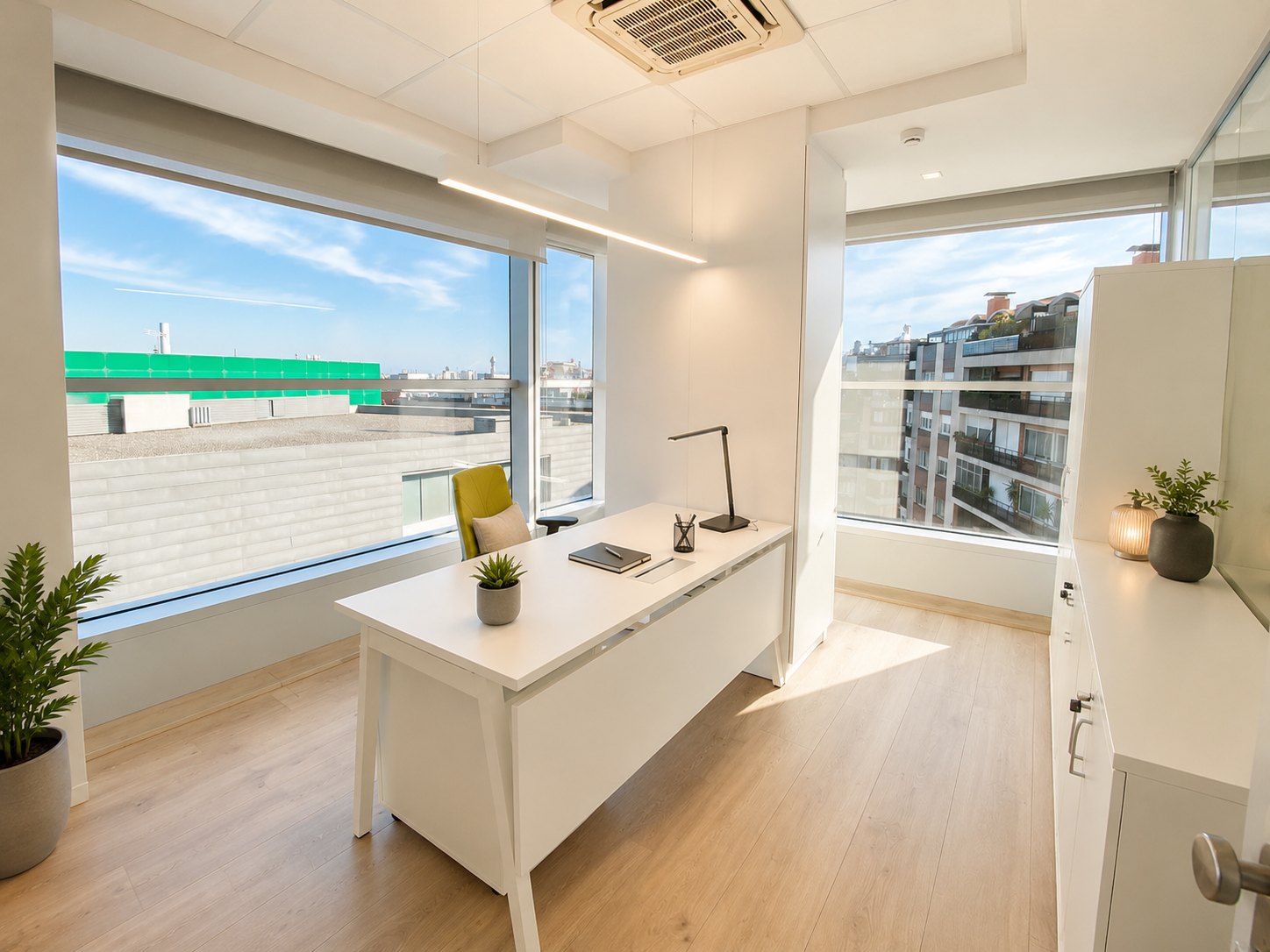 An office glazed on two sides: a white desk in the corner, façade windows on both sides, a suspended linear fitting above