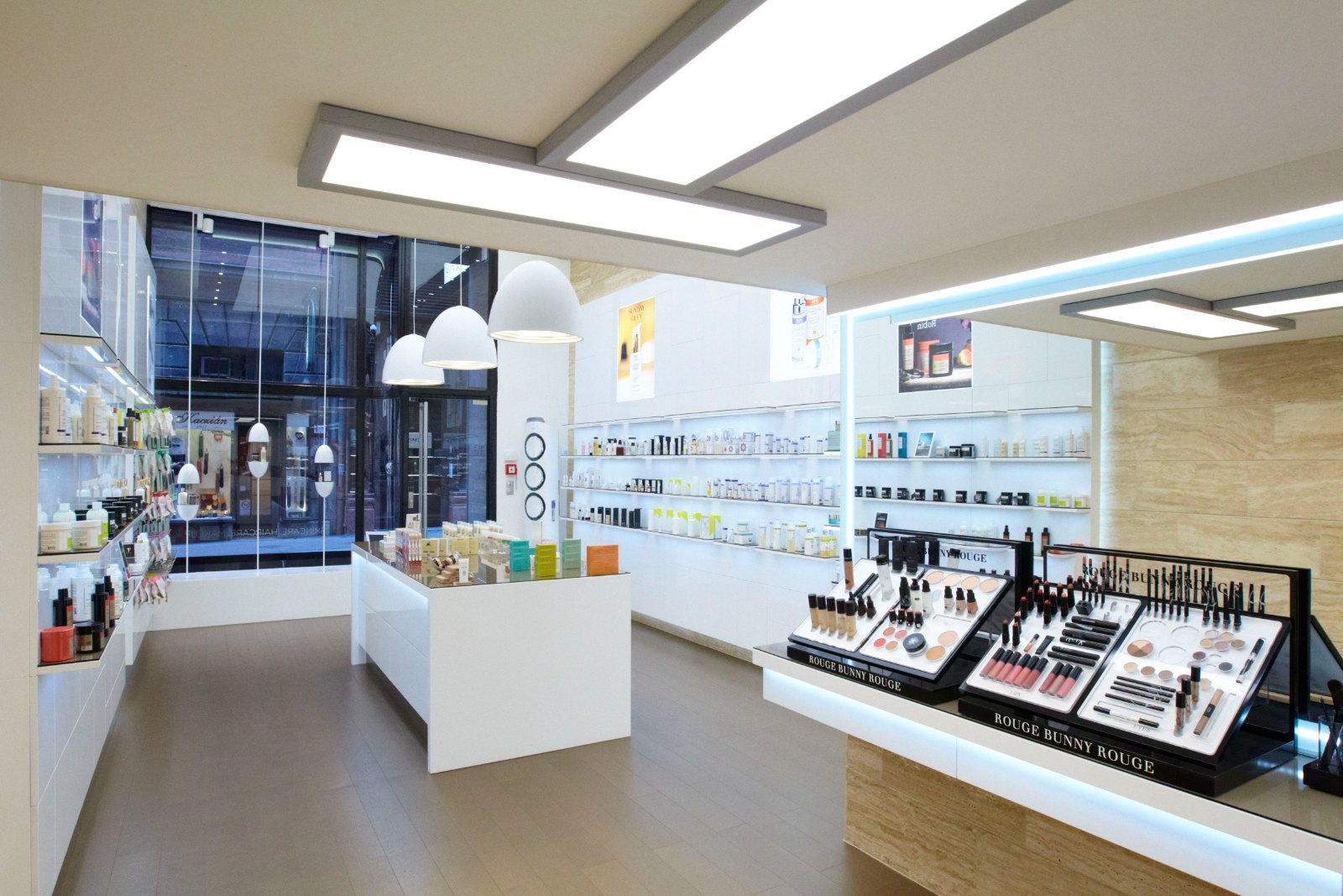 Interior of the Tinamu cosmetics shop with a white island counter, backlit shelves and a band of travertine